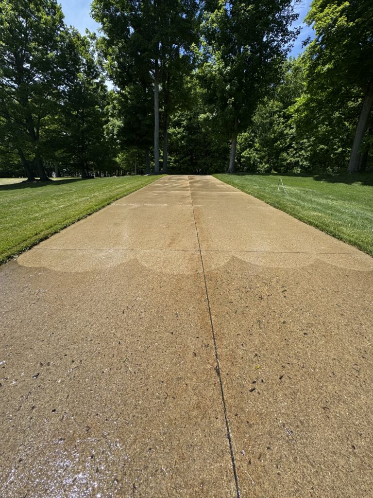 Concrete park path extends toward a tree-lined area, flanked by green lawns under a bright blue sky.