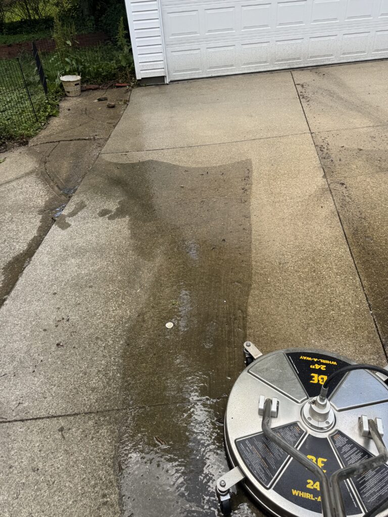 Wet concrete driveway in front of a white garage door before and after pressure washing by Wiley's Pressure Washing Services in Madison, OH