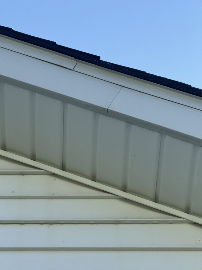 White metal siding and eaves of a building with a black roof edge after being cleaned by Wiley's pressure washing services in Madison, OH