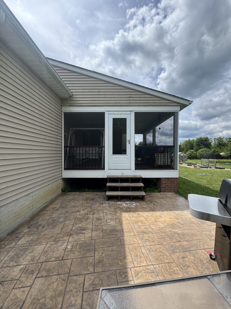 Patio area beside a beige house with a screened porch entrance and wooden steps Being cleaned by Wiley's Pressure Washing Services in Madison, OH