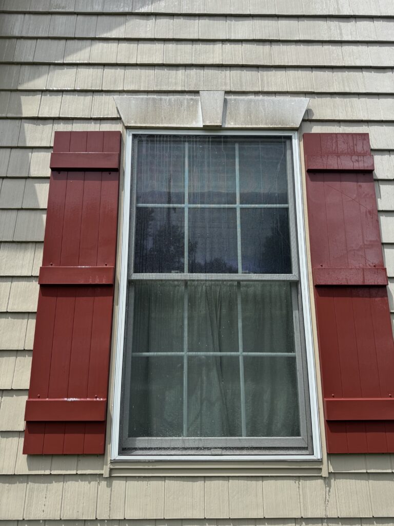 Exterior window with a white decorative awning/overhang above beige siding, rain streaks on the glass windowpane before cleaning from Wiley's Pressure Washing Services in Madison, OH