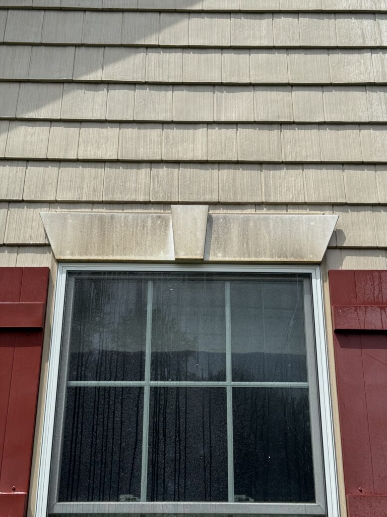 Exterior window with a white decorative awning/overhang above beige siding, rain streaks on the glass windowpane before cleaning from Wiley's Pressure Washing Services in Madison, OH