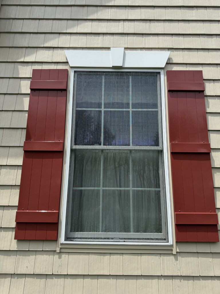 Exterior window with a white decorative awning/overhang above beige siding, rain streaks on the glass windowpane after cleaning from Wiley's Pressure Washing Services in Madison, OH