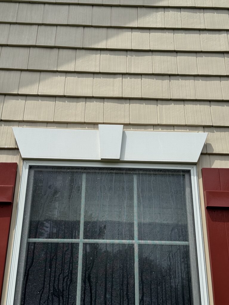 Exterior window with a white decorative awning/overhang above beige siding, rain streaks on the glass windowpane after cleaning from Wiley's Pressure Washing Services in Madison, OH