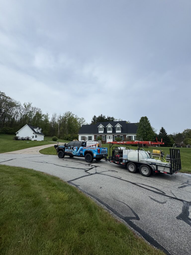 Blue service truck with graphics attached to a trailer carrying equipment and large white tanks, in a suburban neighborhood with houses and trees nearby.
