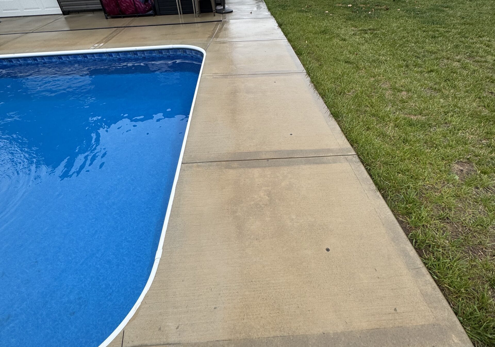 Backyard scene with a blue in-ground pool along a concrete patio; several trucks parked on the grass in the background shown after a cleaning done by wiley's pressure washing services in geneva, oh