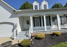 Front view of a white house with a wraparound porch, two dormer windows on the roof, and a mulched front yard under a blue sky. This is in perry, oh and this house was cleaned by wiley's pressure washing services&nbsp;